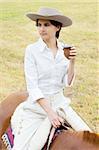 A young Argentinean gaucha relaxing with yerba mate while riding her horse.