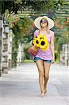 A beautiful young woman walking through a flower covered walkway carrying a basket of sunflowers