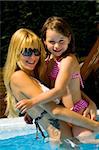 Young blond girl and her sister enjoying the sun in and around the swimming pool