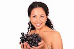 A smiling, happy woman holds two bunches of grapes in her hands, standing on white background.