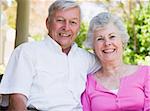 Senior couple smiling at camera sitting on garden seat