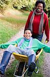 Mother pushing teenage son laying in wheelbarrow