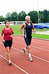 Senior couple running together on a track in a stadium.