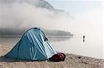 Fisherman standing in a mountain lake with his tent in the foreground