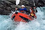 Two people paddling inflatable boat down rapids