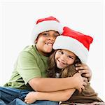 Hispanic brother and sister wearing santa hats hugging