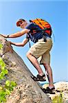 Middle aged man with backpack climbing a rock