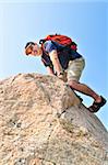 Middle aged man with backpack climbing a rock