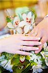 a hand of a groom and a hand of the bride with wedding rings on the flower bouquet