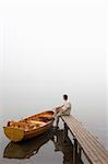 Man sitting on a landing stage at a misty morning in fall