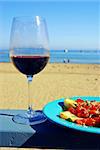 Glass of red wine and plate of fresh bruschetta on a restaurant's deck railing by the ocean beach