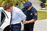 Businessman being handcuffed and placed under arrest in front of his home.