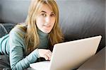 A close shot of a young woman relaxing with her laptop at home, looking at the camera