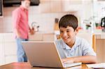 Young boy in kitchen with laptop and paperwork smiling with man