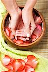 Hands relaxing in bowl of water with rose petals. French manicure.