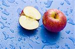 Half and whole red apple on wet blue surface