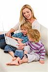 A young mother and her two children using a laptop at home on a settee