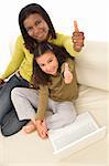 A beautiful young African American mother and her mixed race young daughter using a laptop at home and giving a thumbs up