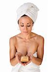 Portrait of ethnic female wrapped in white bath towel around her body and head and holding bar of soap in her palm