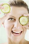 smiling woman holding cucumber-slices in front of her eye