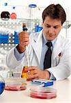 A male scientist, pharmacist or researcher using a pipette to take a sample fluid from erlenmeyer flask in a laboratory.