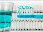 A blue toothbrush with toothpaste, a glass full of mouthwash and towels on the background.