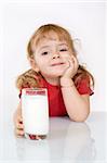 Happy little girl leaning toward the table holding a glass of milk