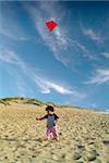 boy on beach playing with a red kite