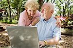 Senior couple enjoying the computer outdoors in a natural setting.