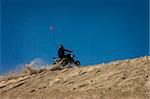 Action shot of an ATV rider riding quad up hill with the blue sky in the background.