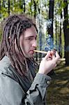 Young man with dreadlock hair smokes pipe.