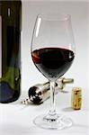 a glas of red wine and a wine bottle, the cork and the corkscrew