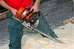 Close up of a woodcarver creating a sculpture from a pine log, using a chainsaw. Sawdust flying.