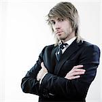 Serious young businessman with shoulder length blond hair, standing with his arms folded.  Isolated on white background.