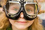 The ridiculous little girl with long hair and grey eyes in motorcycle glasses close up