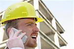 Man with helmet talking on a cell phone in front of a building construction