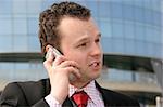 Young businessman smiling and talking on a cell phone in front of a corporate building