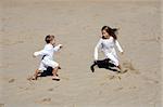 Brother and sister happily running in the sand at the beach in a beutiful sunny day
