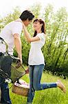 couple in park with holding picnic basket, kissing. Woman raises her leg