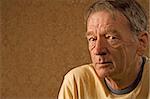 Man with a craggy face wearing a yellow shirt against a gold background with copy space