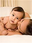 Mom and son lying down on bed and mother embracing the infant baby, who looks at camera with serious facial expression