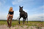 blond teenager and her black horsewalkin  in the nature