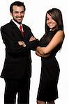 Two business people man wearing black business suit woman in black formal dress with arms crossed and friendly smiles over white