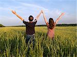 Young Couple in Field Holding Hands Up Rear View