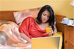 pretty woman working in bed with laptop and drinking orange juice with red shirt