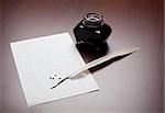 Ink, quill and an empty, splodged page on brown desk