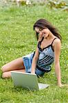 cute brunette in casual dress on the grass  working on the computer