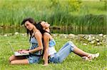 deux fille belle assis sur l'herbe dos à dos, un travail sur ordinateur portable autre au repos