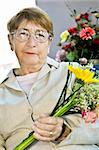 Elderly woman with glasses holding flowers and smiling