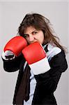 businesswoman wearing boxing gloves with confident attitude. grey background.